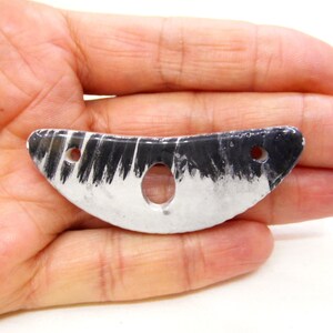 May include: A white and black ceramic pendant with a crescent shape and two holes. The pendant has a black and white striped pattern.