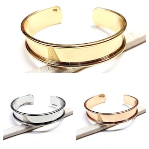 May include: Three metal bangles in gold, silver, and rose gold. Each bangle has a wide band with a slightly raised edge.