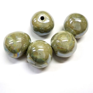 Könnte beinhalten: Sechs irisierende grüne Keramikperlen mit glatter, glänzender Oberfläche. Die Perlen sind rund und haben eine leicht ovale Form.