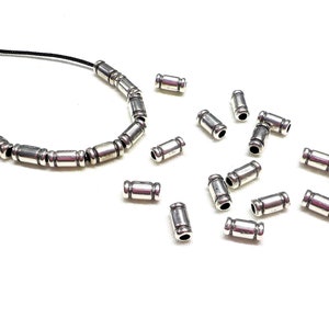 Op de afbeelding: Een zilveren ketting met een zwart koord en zilveren tonvormige kralen. Er zijn ook losse zilveren tonvormige kralen verspreid rond de ketting.