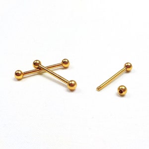 Può includere: Tre pezzi di gioielleria per piercing corporeo a forma di barra dorata. Due barre sono incrociate l'una sull'altra, e una barra è posizionata orizzontalmente. Ogni barra è dotata di due sfere dorate alle estremità.