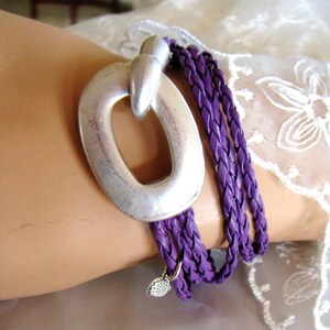 May include: A purple braided leather wrap bracelet with a silver oval charm. The charm has a large open circle in the center.