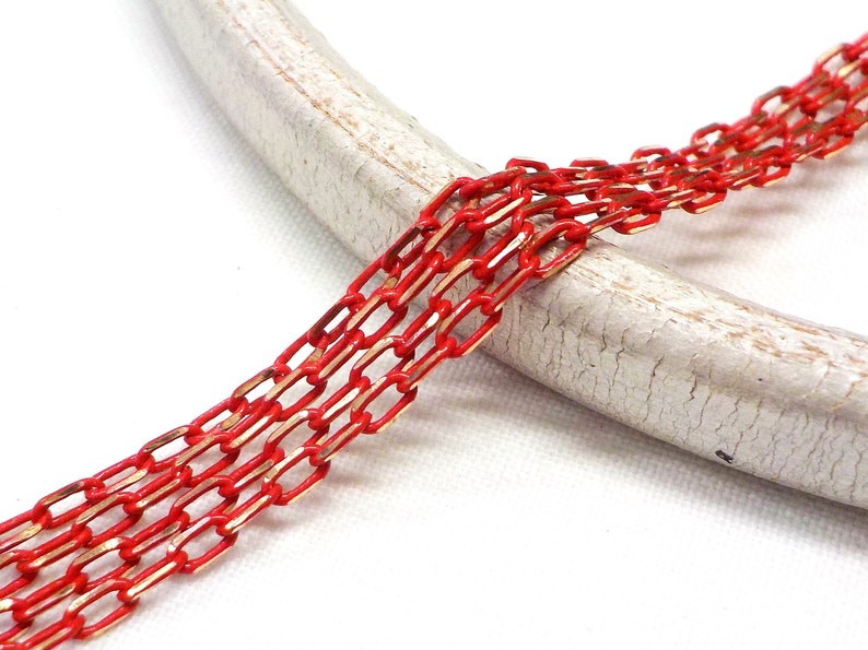 K&ouml;nnte beinhalten: Rote und goldene Kette mit rechteckigem Gliederdesign. Die Kette liegt auf einer wei&szlig;en, strukturierten Oberfl&auml;che.