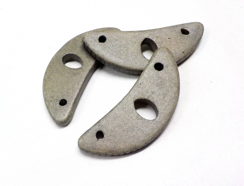 May include: Three gray ceramic crescent moon shapes with holes in them.