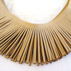 May include: A close-up of a brown suede fringe trim. The fringe is cut into long, thin strips and is arranged in a semi-circle.