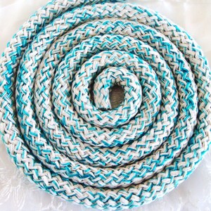 Puede incluir: Primer plano de una cuerda trenzada blanca y turquesa enrollada en espiral. La cuerda está hecha de un material grueso y duradero y tiene un aspecto decorativo y náutico.