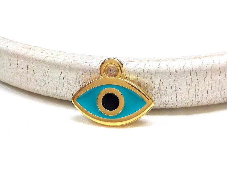 May include: Gold charm with a blue evil eye design. The eye is surrounded by a gold frame and has a black pupil.