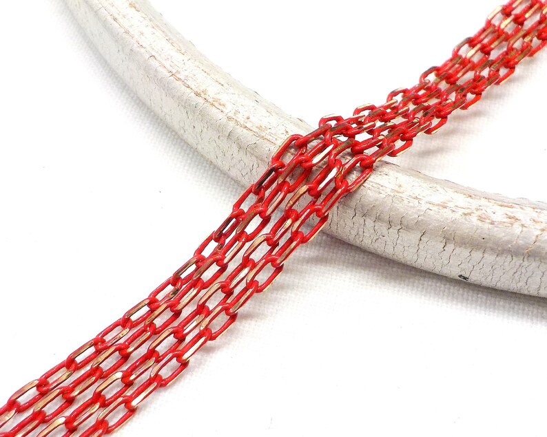 K&ouml;nnte beinhalten: Rote und goldene Kette mit flachem, rechteckigem Glieddesign. Die Kette liegt auf einer wei&szlig;en Oberfl&auml;che.