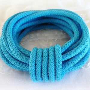 Puede incluir: Primer plano de una cuerda de color turquesa brillante enrollada en un círculo. La cuerda es gruesa y tiene una textura trenzada.