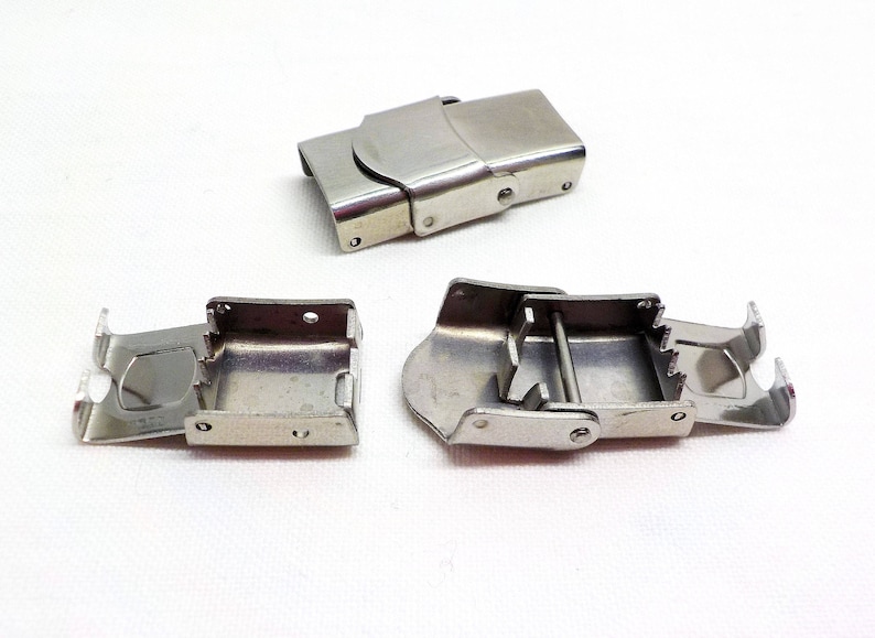 May include: Three silver metal watch band clasps. Two clasps are open and one is closed. The clasps are designed to be used with a watch strap.