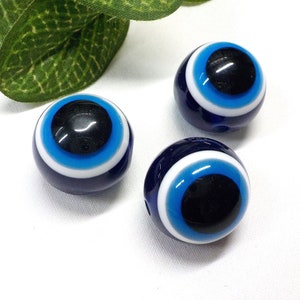 Könnte beinhalten: Drei blaue Glasperlen mit bösem Blick, mit weißen und blauen konzentrischen Kreisen um eine schwarze Mitte. Die Perlen sind rund und haben eine glänzende Oberfläche.