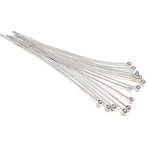 Op de afbeelding: Een bundel zilveren kopspelden met ronde bolle koppen. De spelden zijn in een waaier vorm gerangschikt.