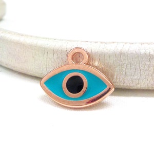Puede incluir: Encanto de ojo turco de oro rosa con un ojo azul turquesa y una pupila negra.