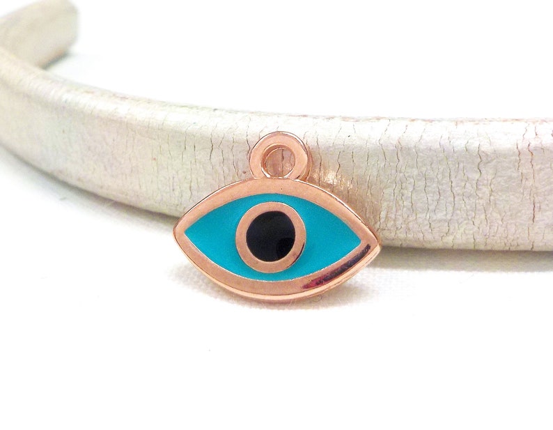 Puede incluir: Encanto de ojo turco de oro rosa con un ojo azul turquesa y una pupila negra.
