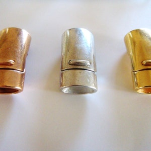 May include: Three metal magnetic clasps in copper, silver, and gold. Each clasp is cylindrical with a rectangular indentation and a magnetic closure. The clasps are designed for jewelry making and crafting.