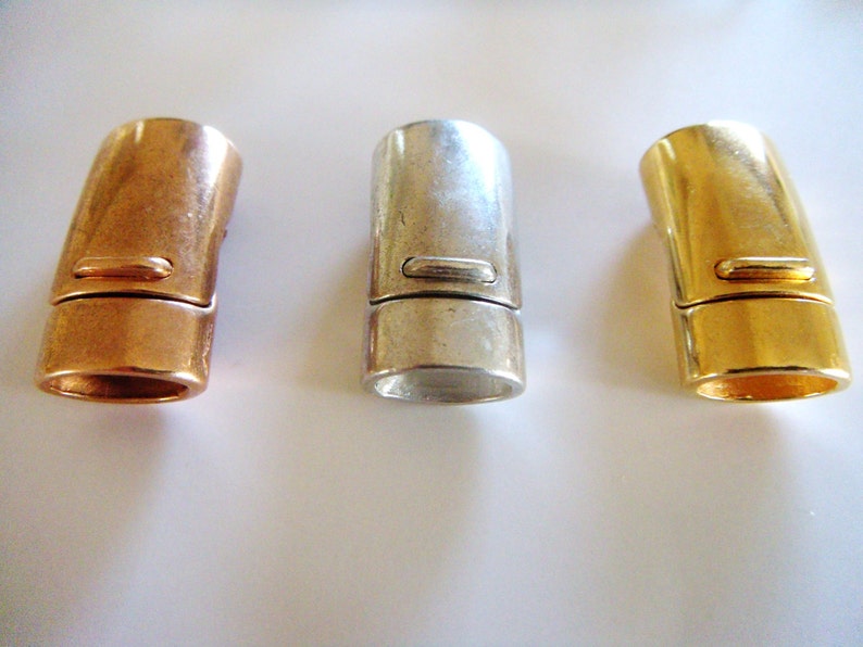 May include: Three metal magnetic clasps in copper, silver, and gold. Each clasp is cylindrical with a rectangular indentation and a magnetic closure. The clasps are designed for jewelry making and crafting.