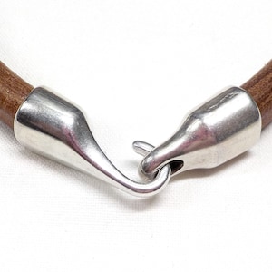 Puede incluir: Un brazalete de cuero marrón con un cierre de gancho plateado.