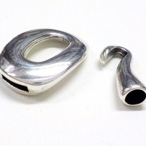 May include: Two silver-toned metal clasps for jewelry making. One clasp is a round oval shape with a small opening. The other clasp is a hook shape with a black interior.