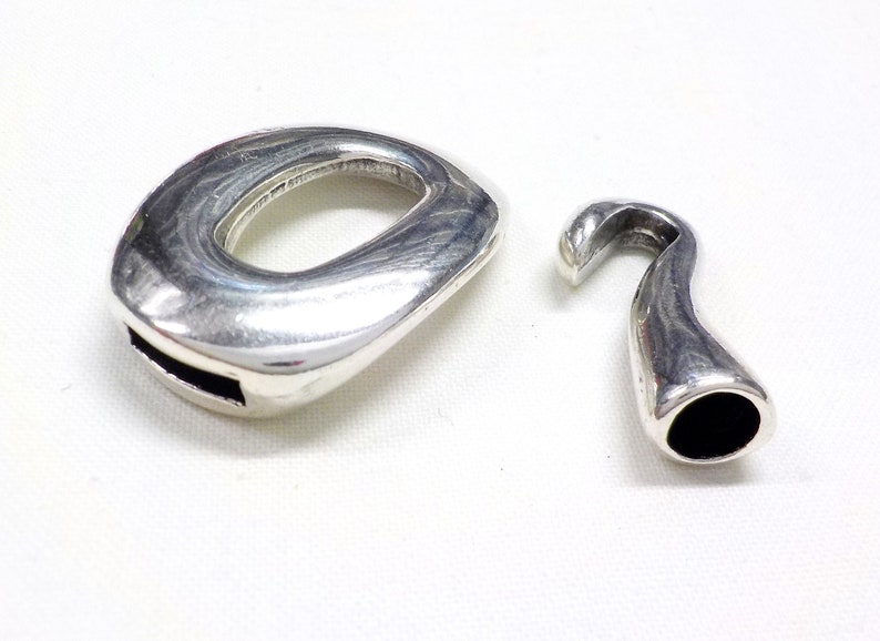 May include: Two silver-toned metal clasps for jewelry making. One clasp is a round oval shape with a small opening. The other clasp is a hook shape with a black interior.