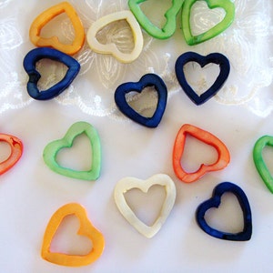 May include: Assortment of colorful heart-shaped beads made of mother of pearl. The beads are in shades of blue, green, orange, and white.