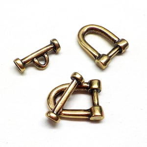 Pode incluir: Três fechos de metal dourado, dois são em forma de D com um pino e um é uma barra reta com um laço.