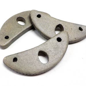 May include: Three gray ceramic crescent moon shapes with holes in the center. The shapes are stacked on top of each other.