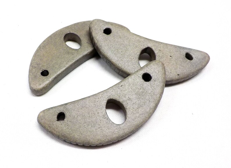 May include: Three gray ceramic crescent moon shapes with holes in the center. The shapes are stacked on top of each other.