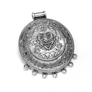 May include: Silver pendant with a detailed floral design and a loop for hanging. The pendant has a circular shape with a textured border.