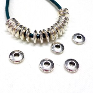 May include: Silver jump rings with a smooth, shiny finish. The rings are arranged in a circle around a green leather cord.