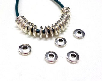 Puede incluir: Anillos de salto de plata con un acabado liso y brillante. Los anillos están dispuestos en un círculo alrededor de un cordón de cuero verde.