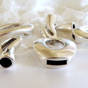 May include: Four silver metal charms with different shapes and designs. The charms have a smooth, polished finish and are designed to be used for jewelry making.
