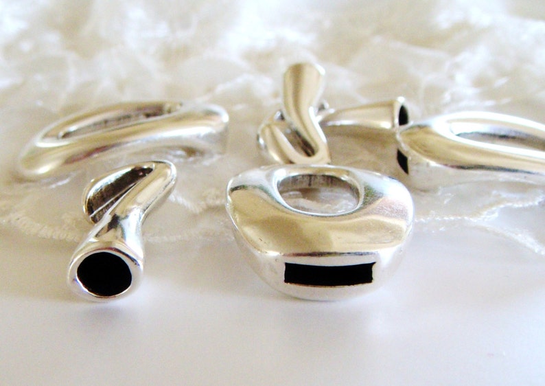 May include: Four silver metal charms with different shapes and designs. The charms have a smooth, polished finish and are designed to be used for jewelry making.