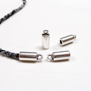 May include: Four silver metal cord end caps with a loop on one end. The cord end caps are cylindrical in shape.