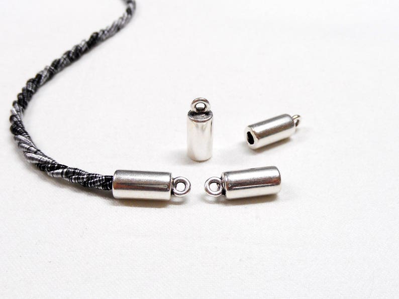 May include: Four silver metal cord end caps with a loop on one end. The cord end caps are cylindrical in shape.