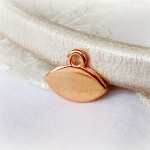 Puede incluir: Un peque&ntilde;o charm de metal de color oro rosa en forma de l&aacute;grima con un bucle en la parte superior.
