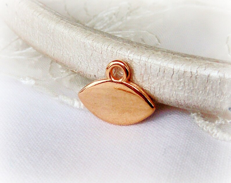 Puede incluir: Un peque&ntilde;o charm de metal de color oro rosa en forma de l&aacute;grima con un bucle en la parte superior.