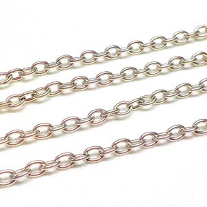 May include: Four strands of silver chain, each with oval links, are laid out on a white surface.