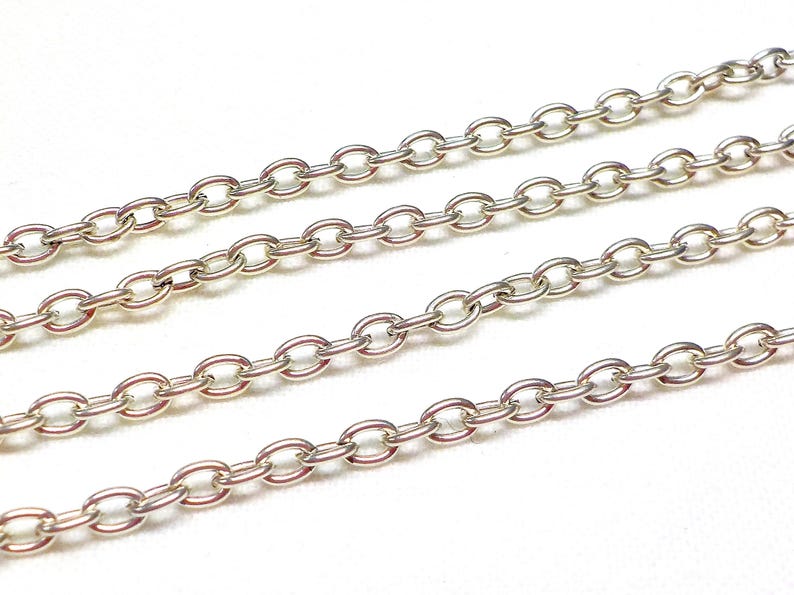 May include: Four strands of silver chain, each with oval links, are laid out on a white surface.