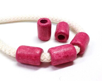Puede incluir: Primer plano de cuentas de madera rosas ensartadas en una cuerda blanca. Las cuentas cilíndricas tienen una superficie texturizada y están espaciadas uniformemente. La cuerda es gruesa y trenzada, creando contraste. Fondo blanco.