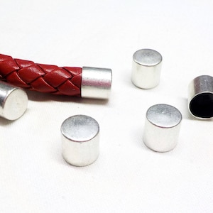 Puede incluir: Cinco tapones de metal plateado para cordón o cuerda de cuero. Los tapones son cilíndricos y tienen un acabado liso y brillante.