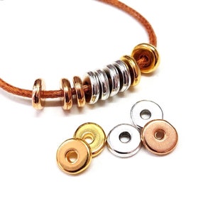 May include: A bracelet featuring a brown cord and a selection of metal beads. The beads are in gold, silver, and rose gold tones. Several loose beads in matching colours are scattered below the bracelet.