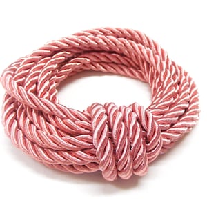 May include: A pink braided rope is coiled into a circle with a knot in the centre.