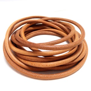 May include: A close-up of a coil of light brown leather cord. The cord is smooth and supple, and it is perfect for crafting projects.