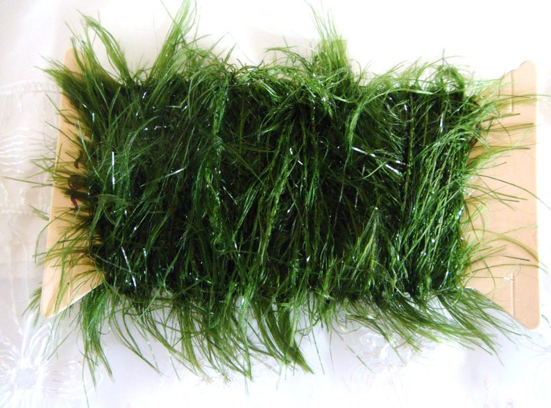 May include: A spool of green tinsel with a silver shimmer. The tinsel is wrapped around a cardboard spool.