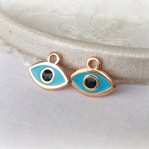 Puede incluir: Dos amuletos de ojo turco dorados con esmalte azul y centros negros. Los amuletos tienen un bucle en la parte superior para sujetarlos a joyas u otras manualidades.