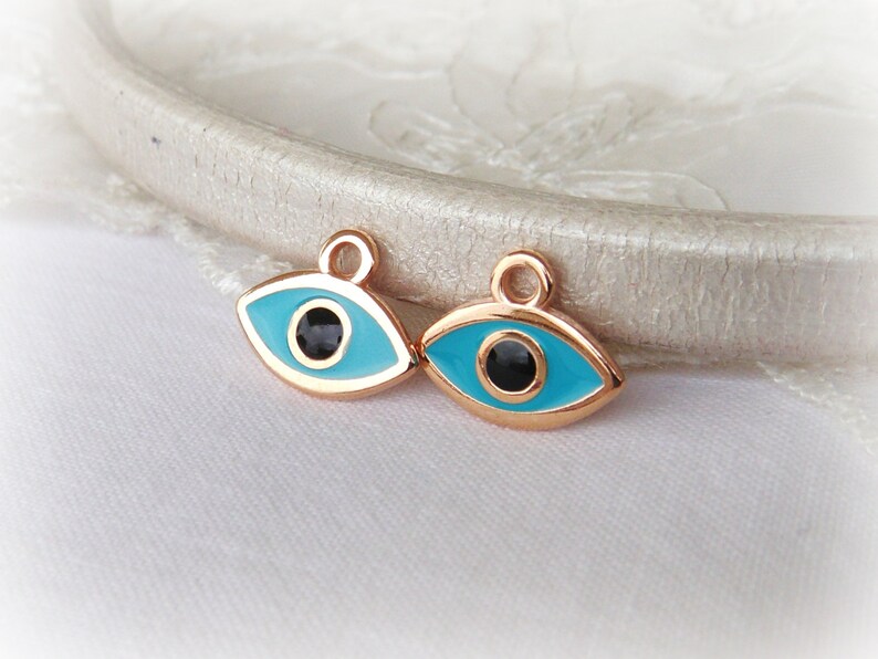 Puede incluir: Dos amuletos de ojo turco dorados con esmalte azul y centros negros. Los amuletos tienen un bucle en la parte superior para sujetarlos a joyas u otras manualidades.