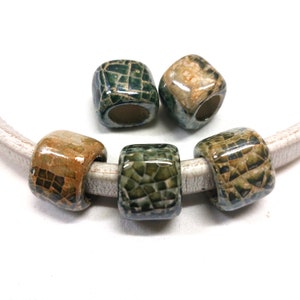 Pode incluir: Quatro contas de cerâmica com um padrão de mosaico em tons de verde, marrom e branco. As contas são de forma quadrada com um furo no centro para enfiar.