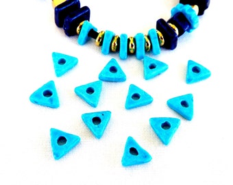 May include: A collection of turquoise blue triangle-shaped beads with a hole in the center. The beads are scattered on a white surface.