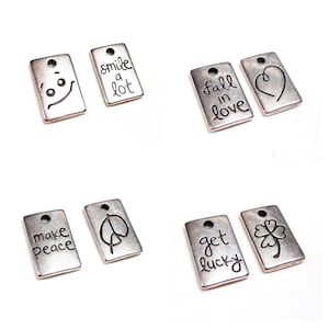 Può includere: Sei ciondoli in argento con diversi detti e disegni. I ciondoli includono "smile a lot", "fall in love", "make peace", "segno di pace", "get lucky" e un quadrifoglio.