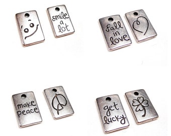 Puede incluir: Seis colgantes de plata con diferentes lemas y diseños. Los colgantes incluyen "smile a lot", "fall in love", "make peace", "signo de paz", "get lucky" y un trébol de cuatro hojas.